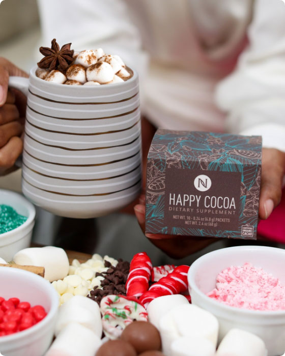 Woman holding Neora’s hottest holiday limited-time must-have, Happy Cocoa, next to a mug with hot cocoa with a display of candy canes, sprinkles and marshmellows.